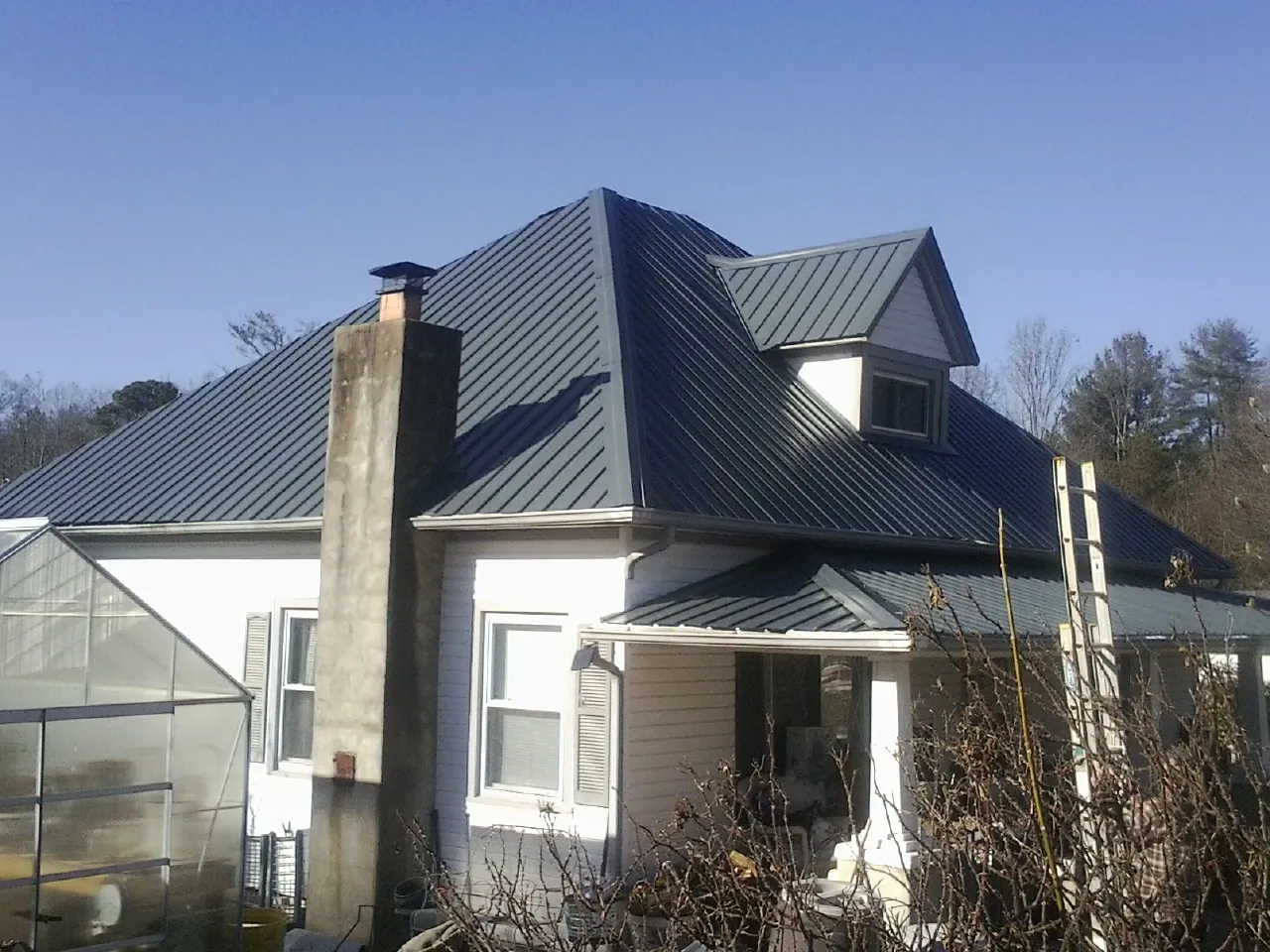 Dark blue standing seam metal roof on a white farmhouse with dormer — Slate & Tile Roof Repair by Roofing Brothers in La Ward