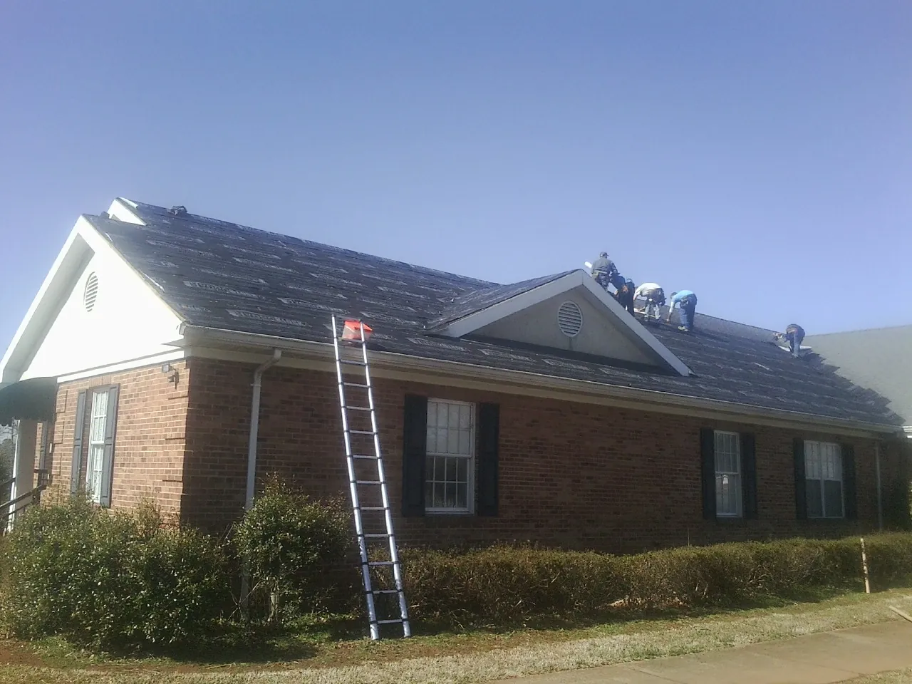 Crew tearing shingles off a brick ranch roof with a ladder set — Emergency Roof Repair work by our crew in La Ward
