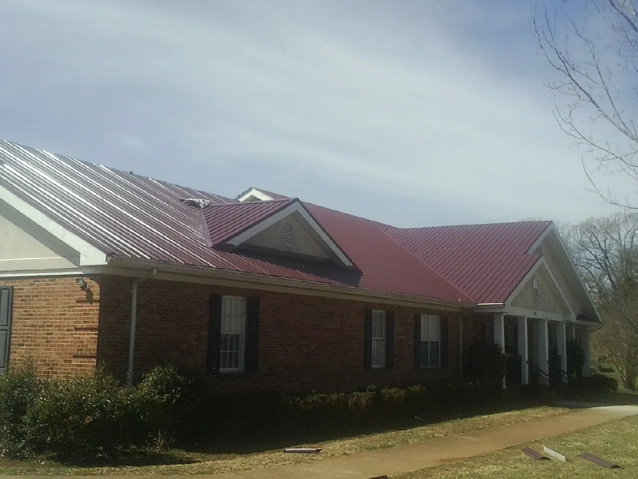 Red metal roof with gabled entries on a long brick building, from a Hail Damage Roof Repair job in La Ward