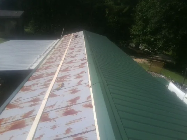 Old rusted panels beside newly installed green metal roofing — Wind Damage Roof Repair by Roofing Brothers in La Ward