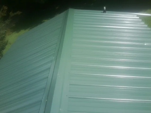 New green metal panels meeting at the ridge of a roof — Flat Roof Repair work by our crew in La Ward