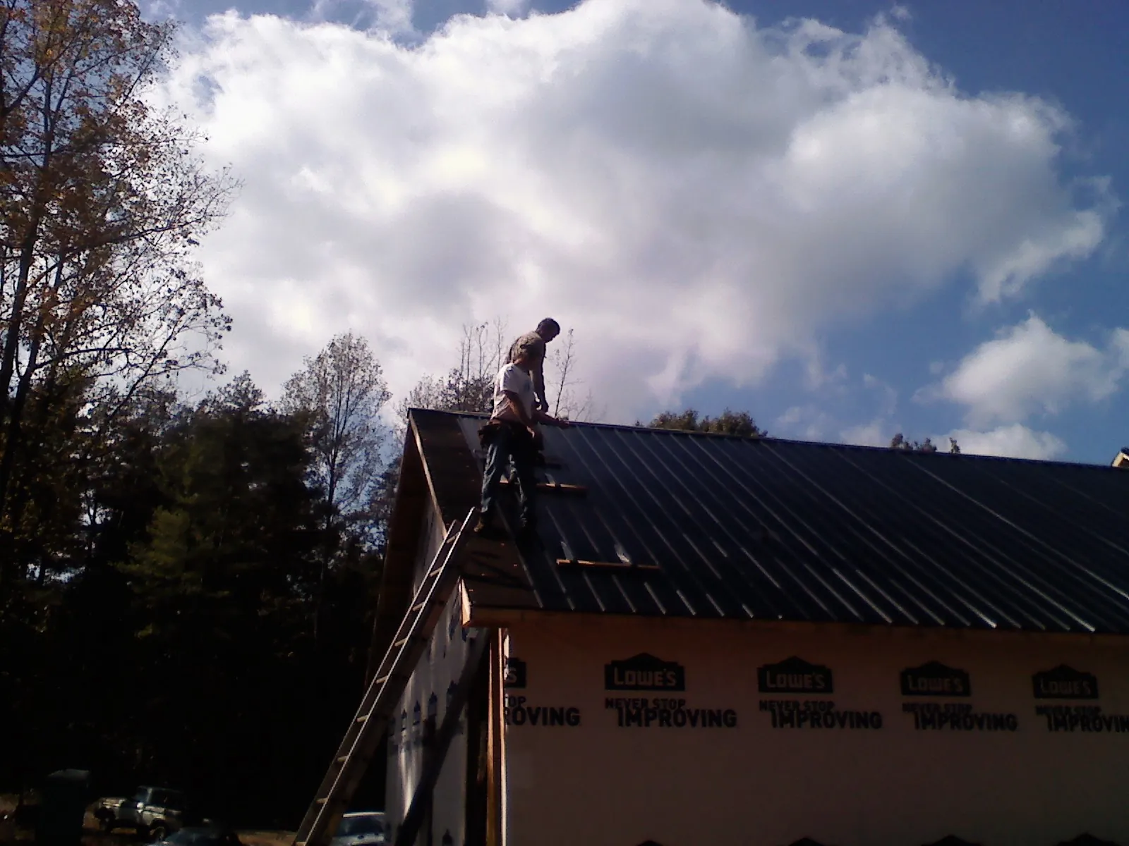 Roofer fastening dark metal panels high against a cloudy sky, from a Roof Inspection job in La Ward
