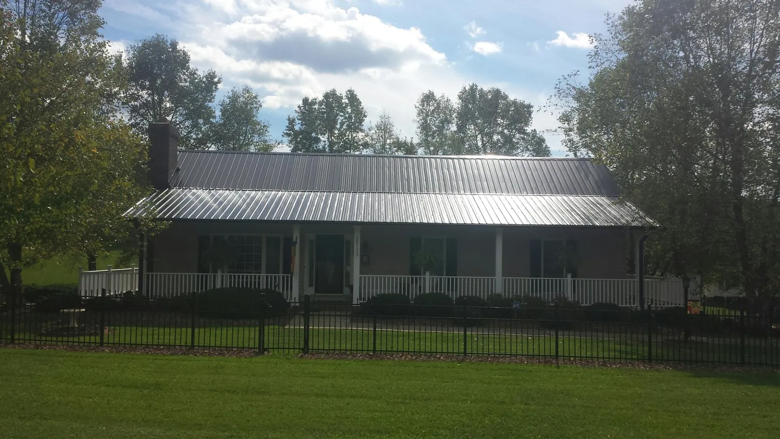 Gray metal roof on a brick ranch with a full width front porch — Gutter Guard Installation work by our crew in La Ward