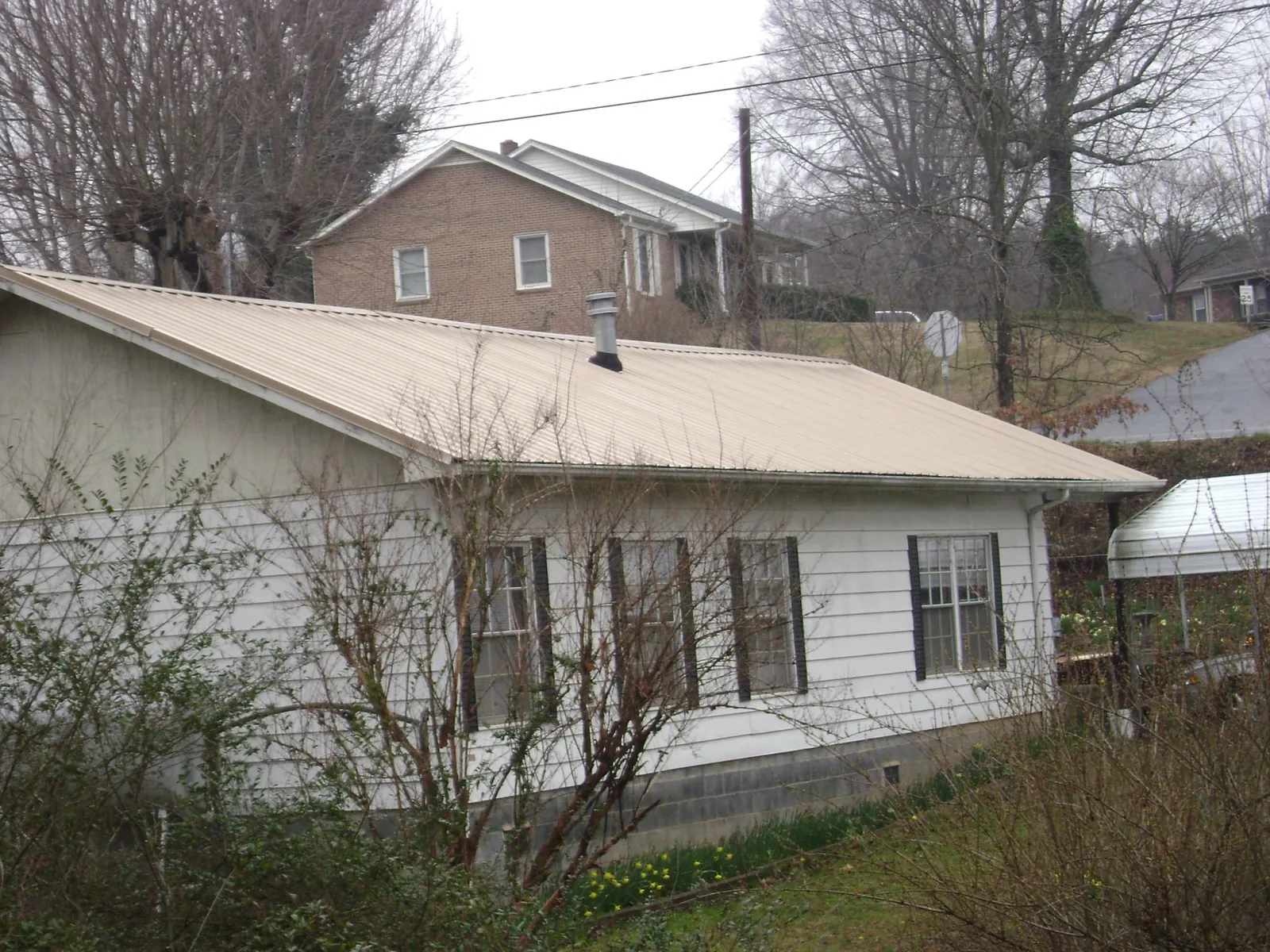 Tan metal roof on a white sided house set into a hillside — Commercial Roofing by Roofing Brothers in La Ward